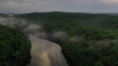 narrow river surrounded by dense forest and rising fog, early morning view