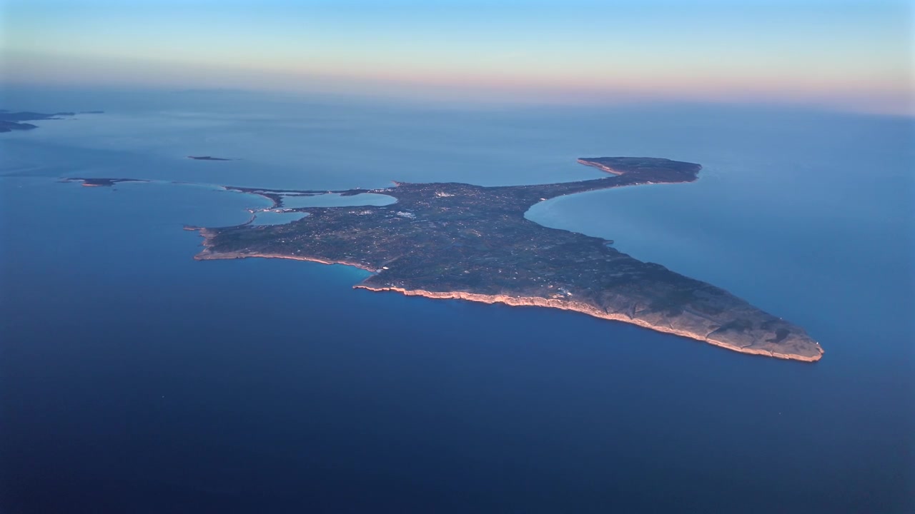 Una veduta aerea rotante dall'alto dell'isola di Formentera (Ibiza), scattata dalla cabina di pilotaggio di un aereo al tramonto, con l'isolotto illuminato dalla luce soffusa del sole calante