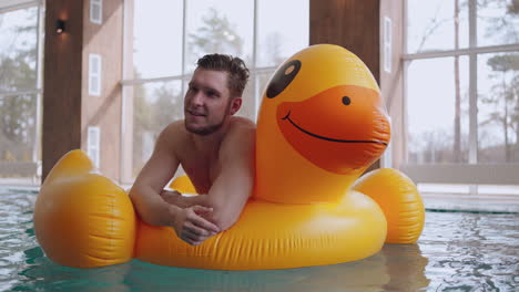 happy caucasian man is relaxing in swimming pool lying on big inflatable duck and floating