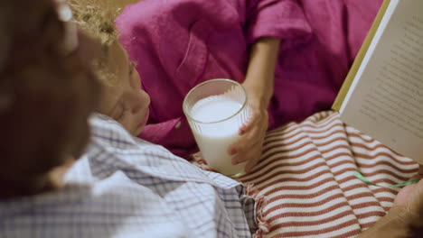 Süßes-Junges-Mädchen,-Das-Milch-Trinkt-Und-Dem-Opa-Beim-Lesen-Zuhört
