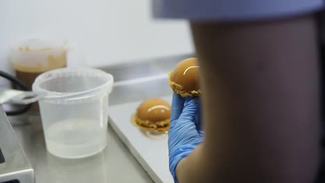 un pastelero con guantes azules pone pasteles esmaltados con caramelo en platos especiales de cartón dorado para ponerlos en la vitrina más tarde. deliciosos postres. hermoso arte gastronómico.