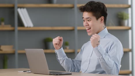 happy asian man celebrating success at laptop