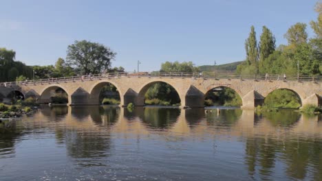 tranquil scene of an ancient stone bridge reflecting in calm water on a sunny day