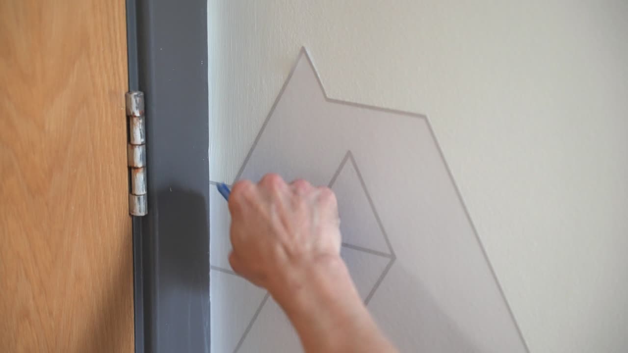 Workman installing vinyl wall graphic on to wall for client with geometric design using squeegee applicator in office space