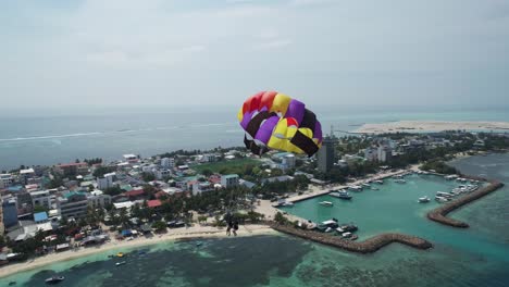 couple on maldives vacation parasailing high over island coast, drone view