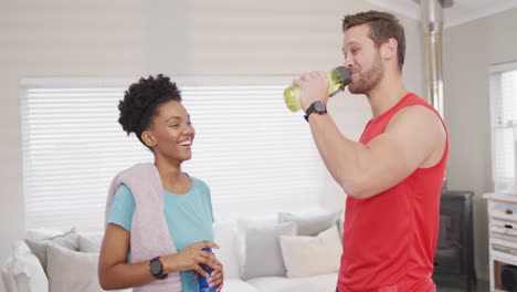 video de una feliz pareja diversa bebiendo agua después del entrenamiento en casa