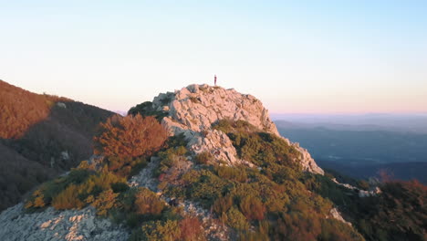 zoom in drone shot of a woman doing yoga on top of a mountain with the first lights of sunrise