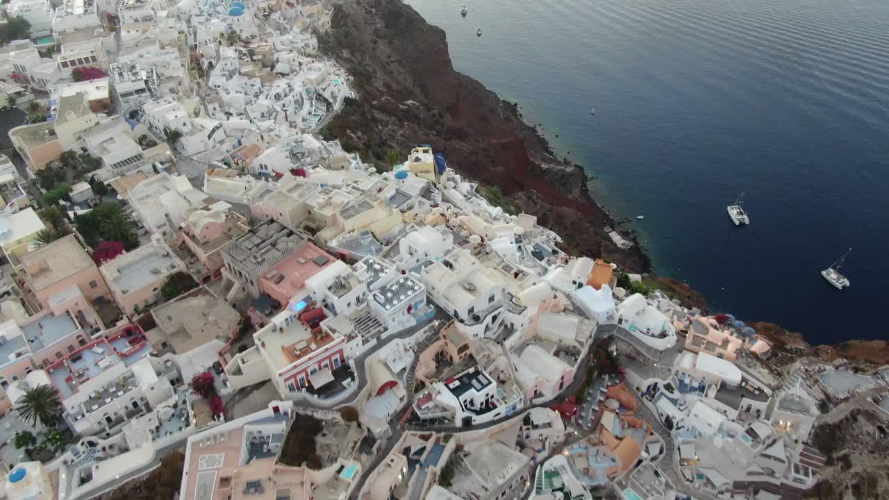 vista de drones en grecia volando sobre santorini con la ciudad de oia vista superior casas blancas y techos azules en un acantilado junto al mar mediterráneo al amanecer