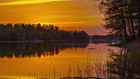 golden sky sunset over water timelapse, with trees and house on the bank of the lake in the evening