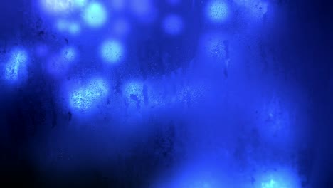 animation of glowing blue bokeh background seen through a wet and dirty glass