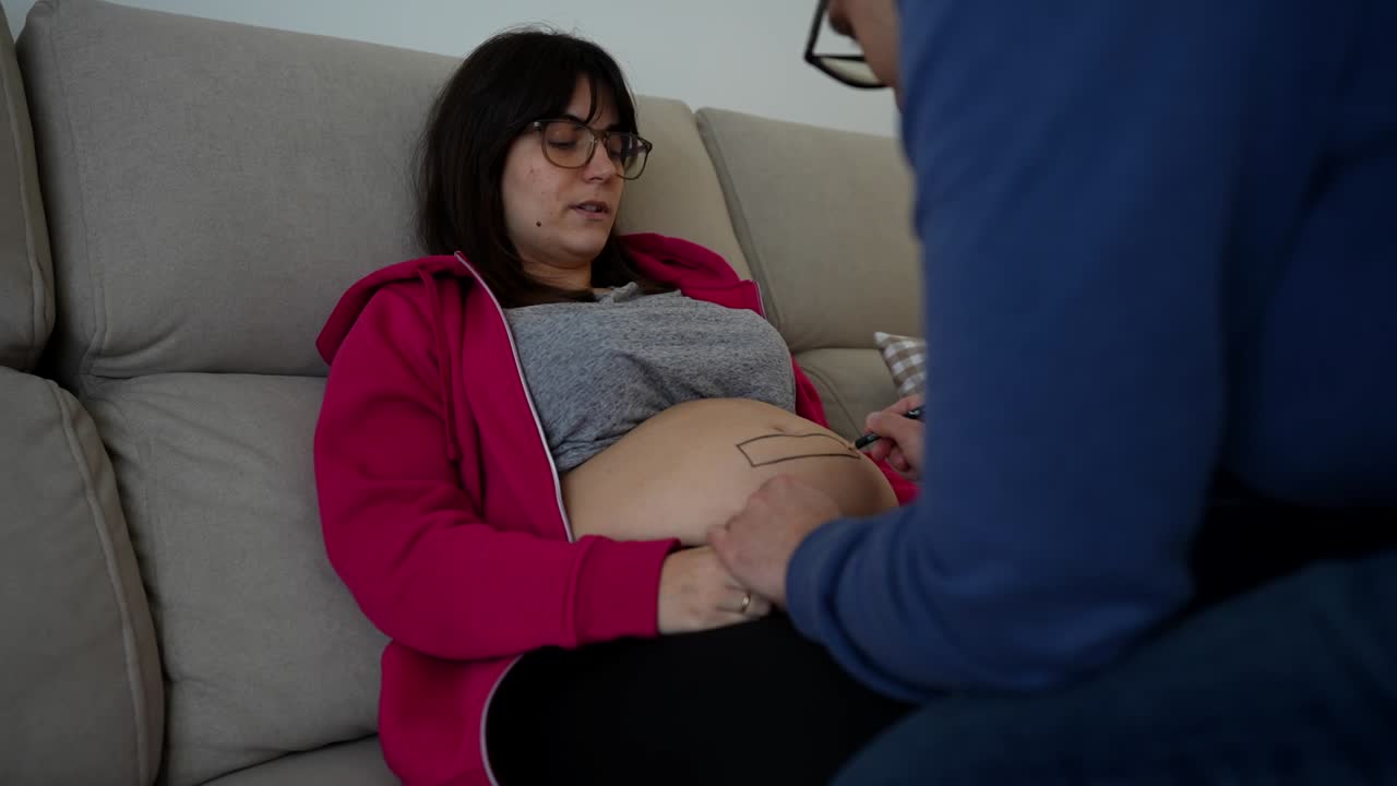 Happy first-time couple painting pregnant woman's belly. Fast motion