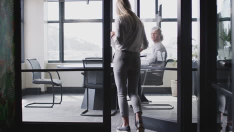 young white woman joins male creative in a meeting room for a job interview, seen through glass wall