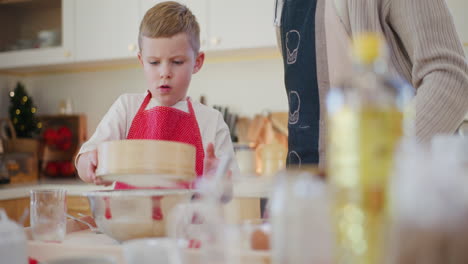 boy helps dad cook and sifts flour while making dough