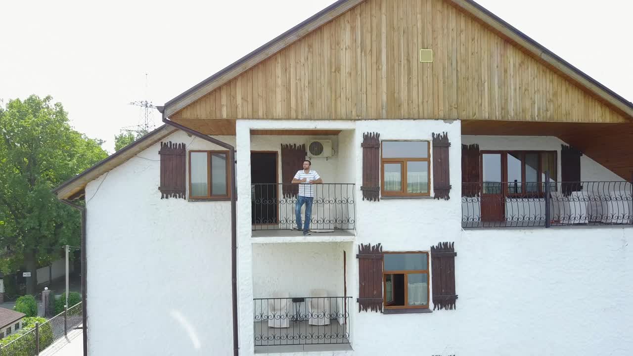 Man Drinking Coffee At Balcony. Young hipster man resting at home balcony with cup of coffee