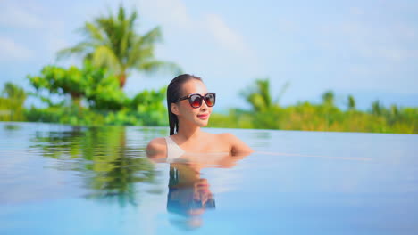 Con-El-Pecho-Alto-En-El-Relajante-Agua-De-La-Piscina,-Una-Mujer-Joven-Mira-El-Paisaje-A-Su-Alrededor.