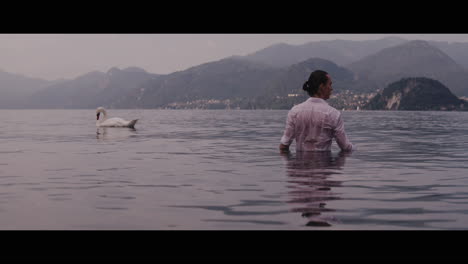 man wading in a lake, swan in the background