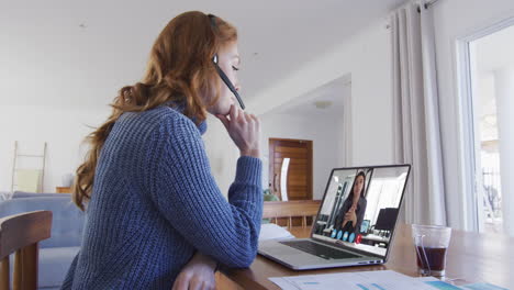 mujer de negocios caucásica sentada en un escritorio usando una computadora portátil haciendo una videollamada con una colega