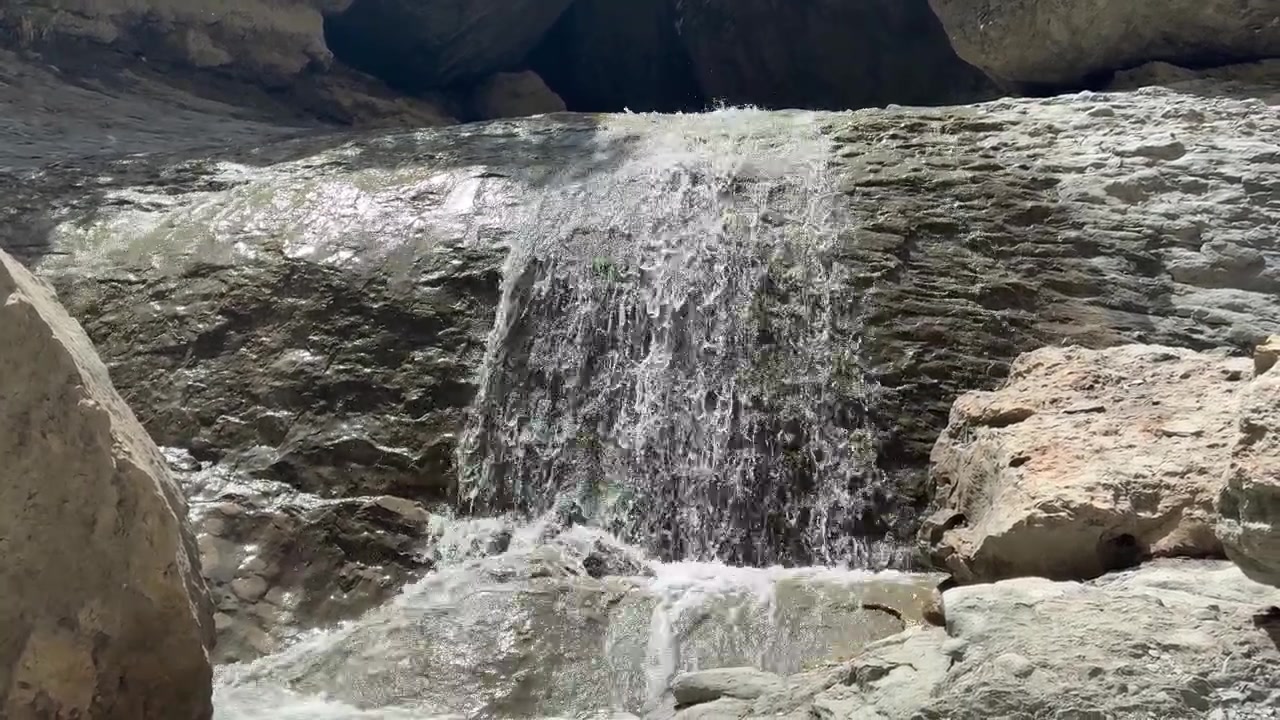 Uma pequena cascata cai sobre uma falésia rochosa no Distrito de Gunibsky, Daguestão, Rússia, com a luz do sol salpicando a água.