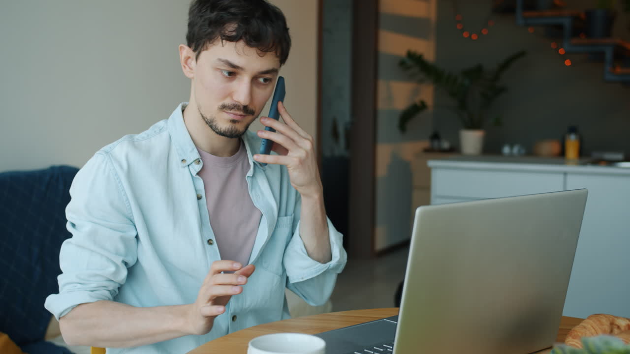 hombre trabajando desde casa en una computadora portátil y una llamada telefónica