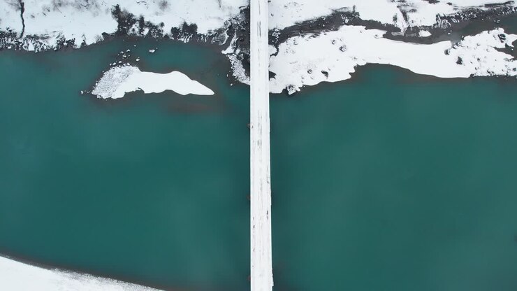 Drone shot of snow covered road over green lake and snow covered landscape