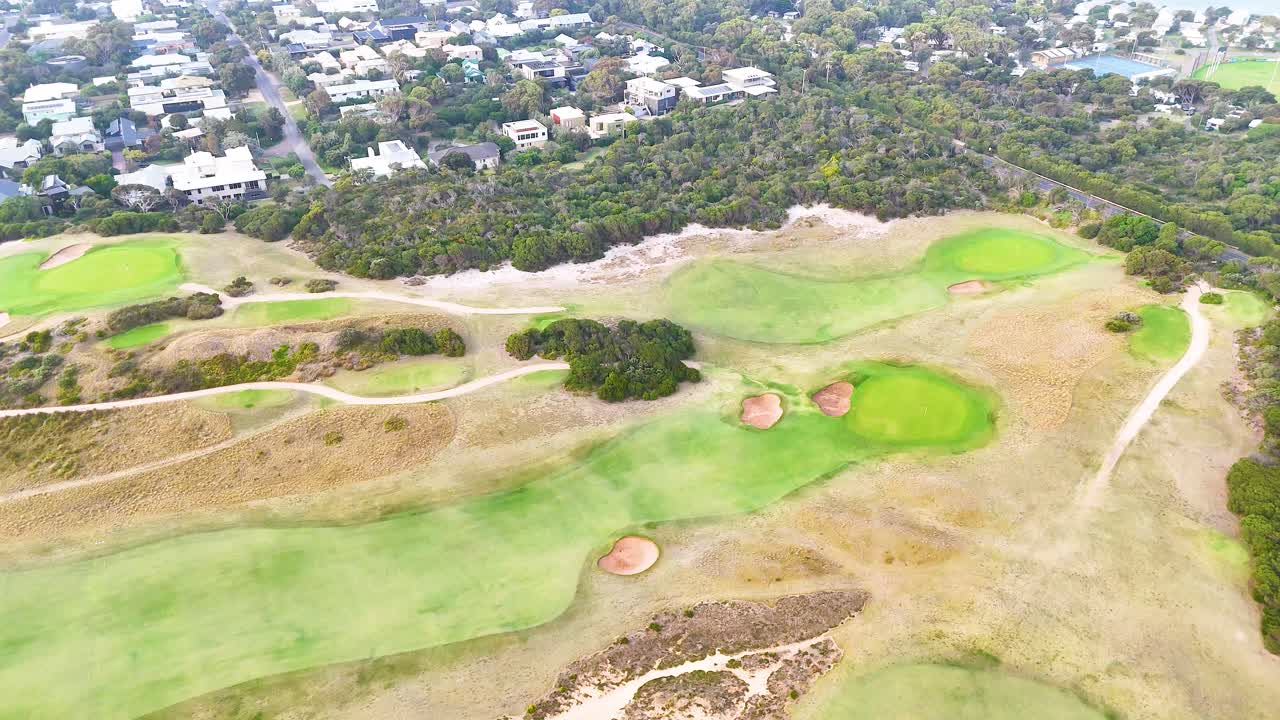 Drone footage captures expansive golf course landscape in Barwon Heads, Australia, under bright daylight with surrounding residential area