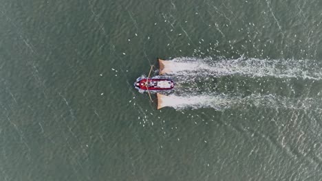 drone topdown shot of a fishers boat dragging the nets thru the water