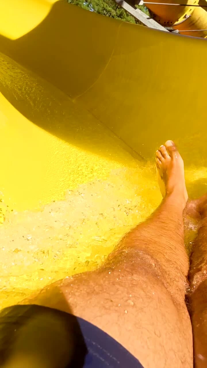 Visuale in prima persona di gambe che scivolano lungo uno scivolo acquatico giallo