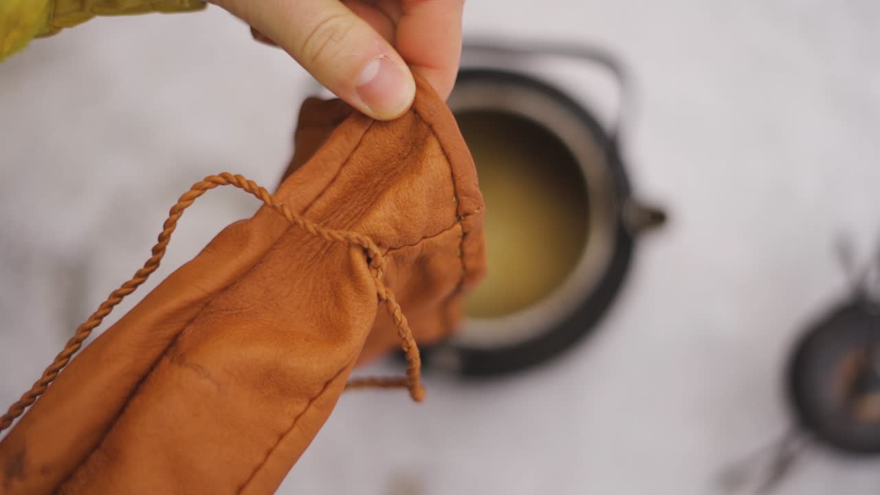 Pouring coffee beans in a kettle in the snow. Making coffee outdoors. Hiking adventure.