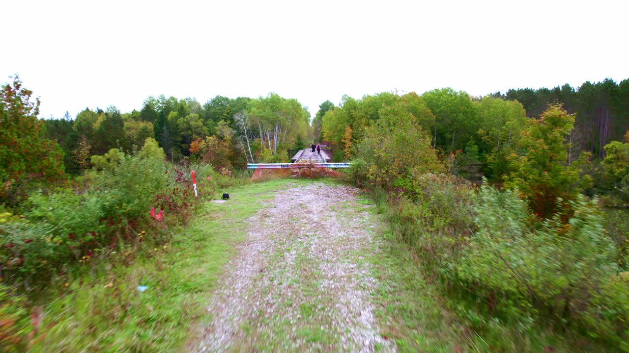 다리 위를 걷는 젊은 부부와 함께 오솔길을 따라 다리 위로 날아가는 드론 샷