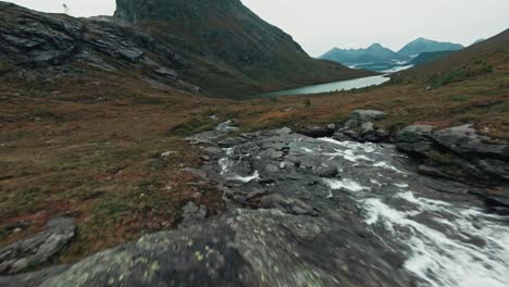 mountain river flowing towards lake in norway, aerial fpv view