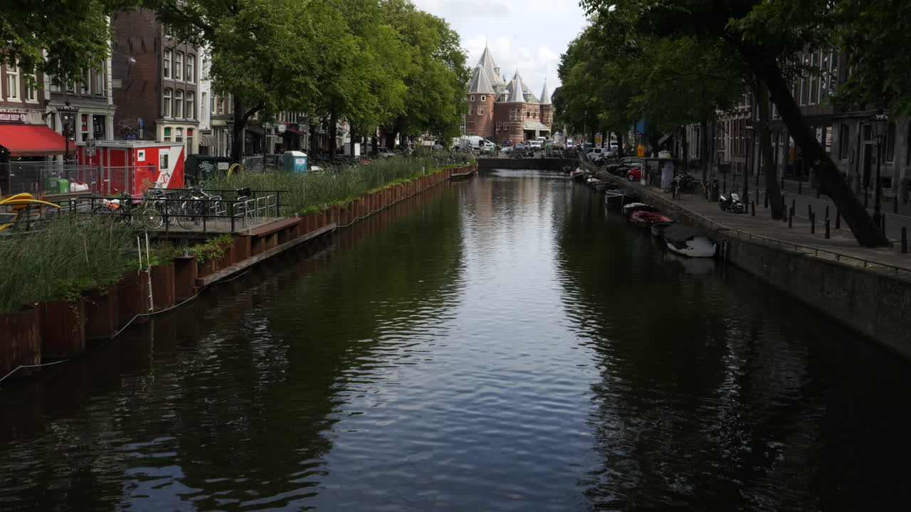 Groenburgwal canal flowing towards the munttoren tower on a cloudy summer day in Amsterdam, Netherlands