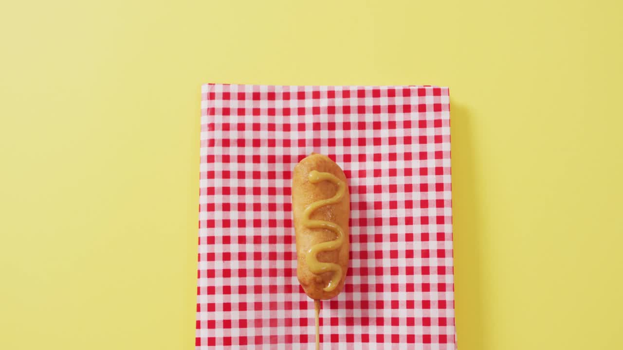 video de un perro de maíz con mostaza en una superficie amarilla