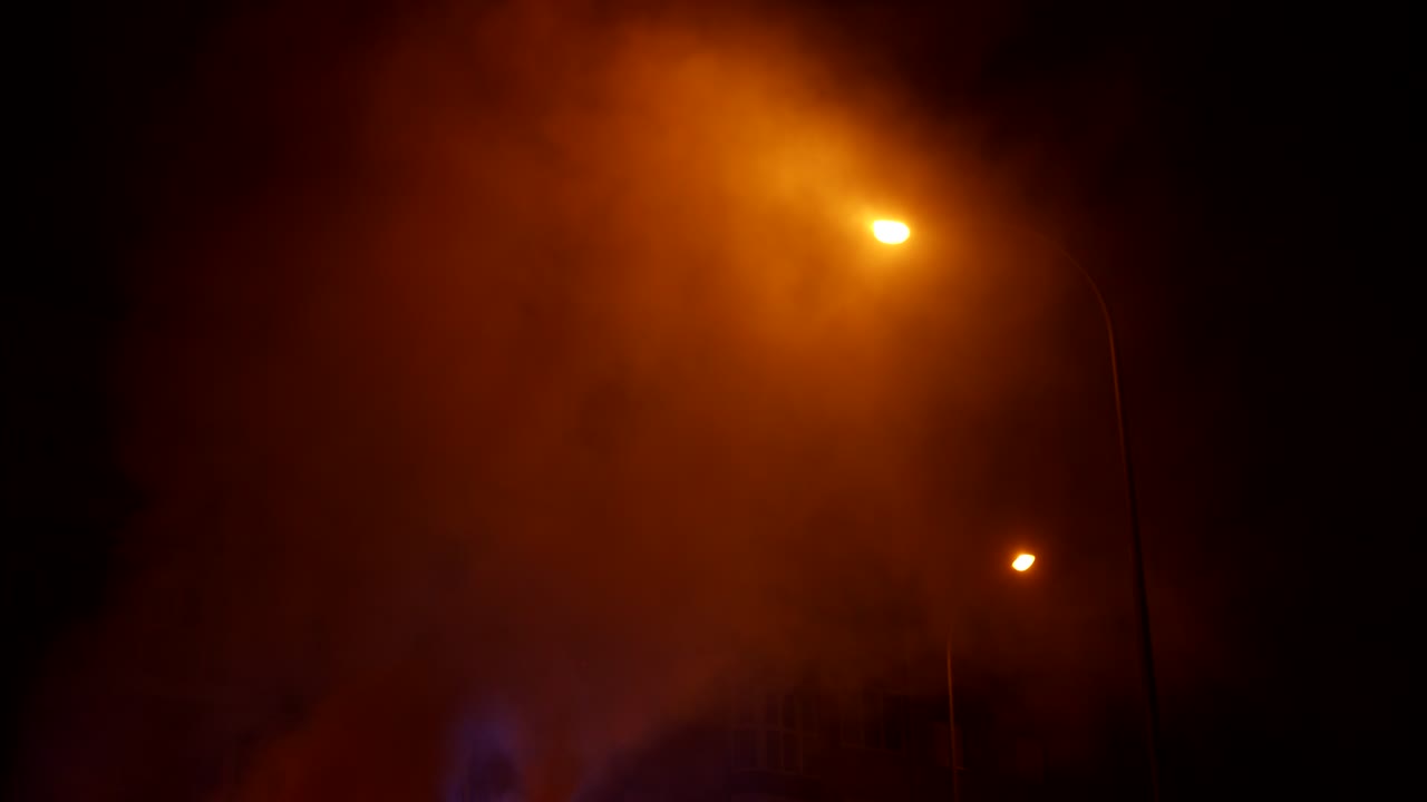 Thick Smoke Billowing at Night Under Orange Streetlights