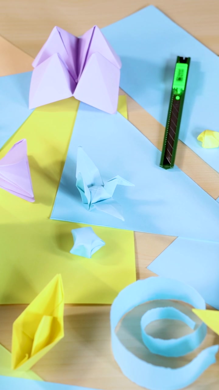 Vari animali e barche di origami disposti su fogli di carta pastello, illuminazione brillante, vista dall'alto.