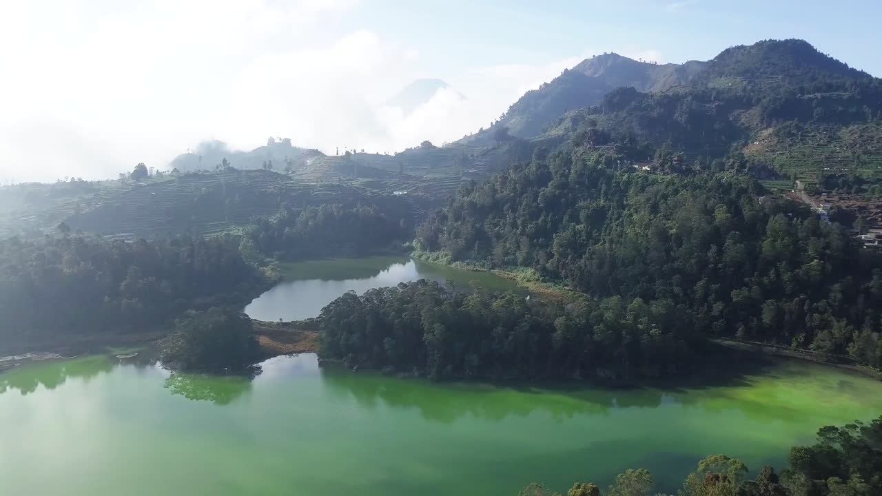 vuelo de drones sobre el lago natural telaga warna rodeado de árboles verdes que crecen en la montaña durante el día soleado