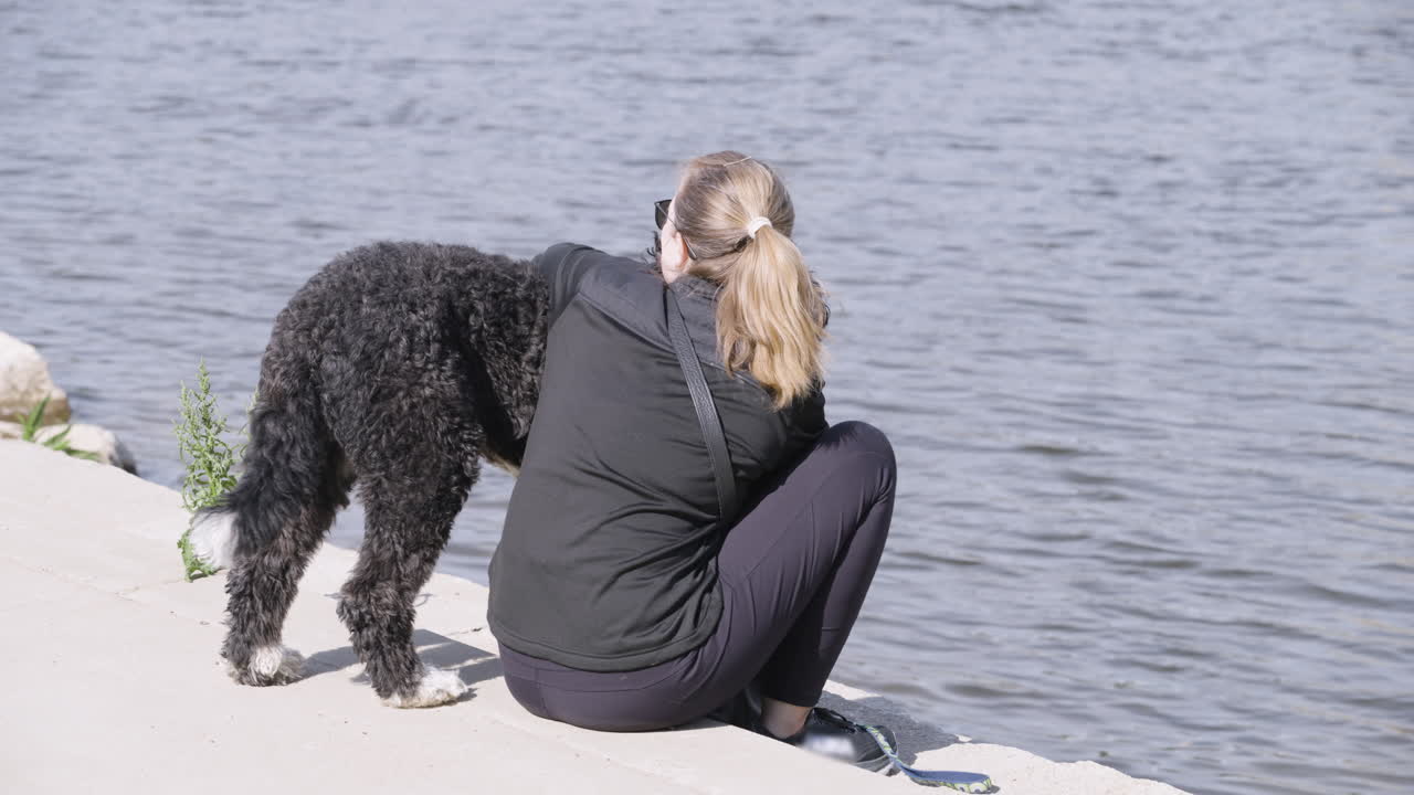 mujer y su perro sentados junto a un río en la ciudad