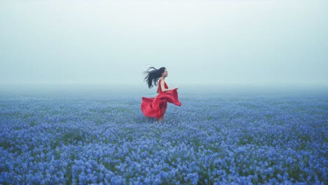 woman in red dress running through a field of blue flowers in fog
