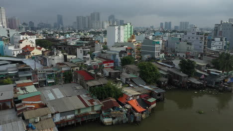 Saigon,-Ho-Chi-Minh-City,-Vietnam-early-morning-sunny-drone-footage-flying-in-over-Kenh-Te-canal-and-district-four-rooftops-with-view-of-city-skyline-and-green-space