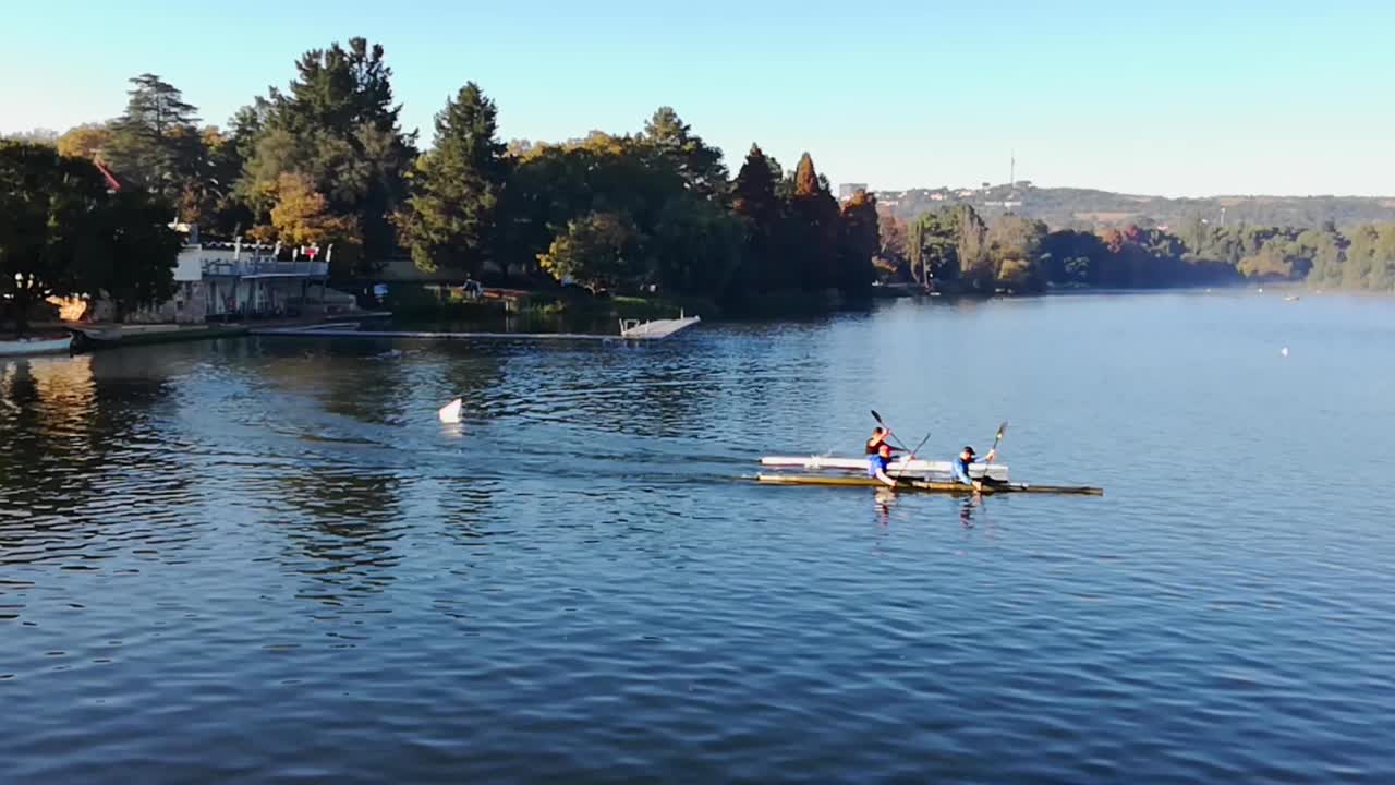 Group of kayakers rowing around a dam early one autumn morning. Still some mist over the water and trees are beginning to go yellow. Wide, Emmarentia dam, Johannesburg Botanical Gardens, South Africa