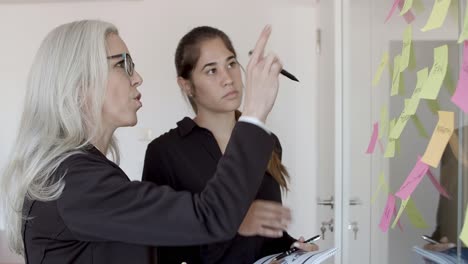 mentor and young employee sticking memos on glass board