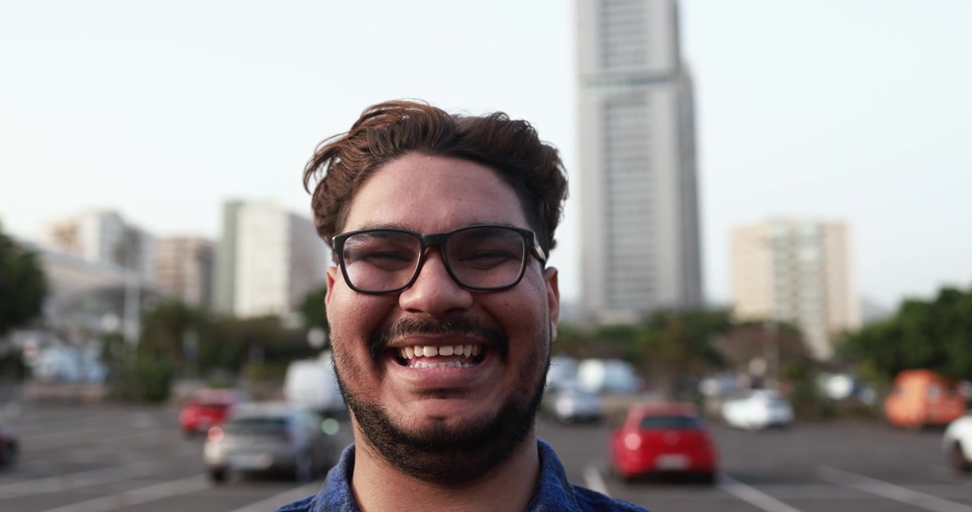Giovane uomo con gli occhiali che sorride e ride in un contesto urbano