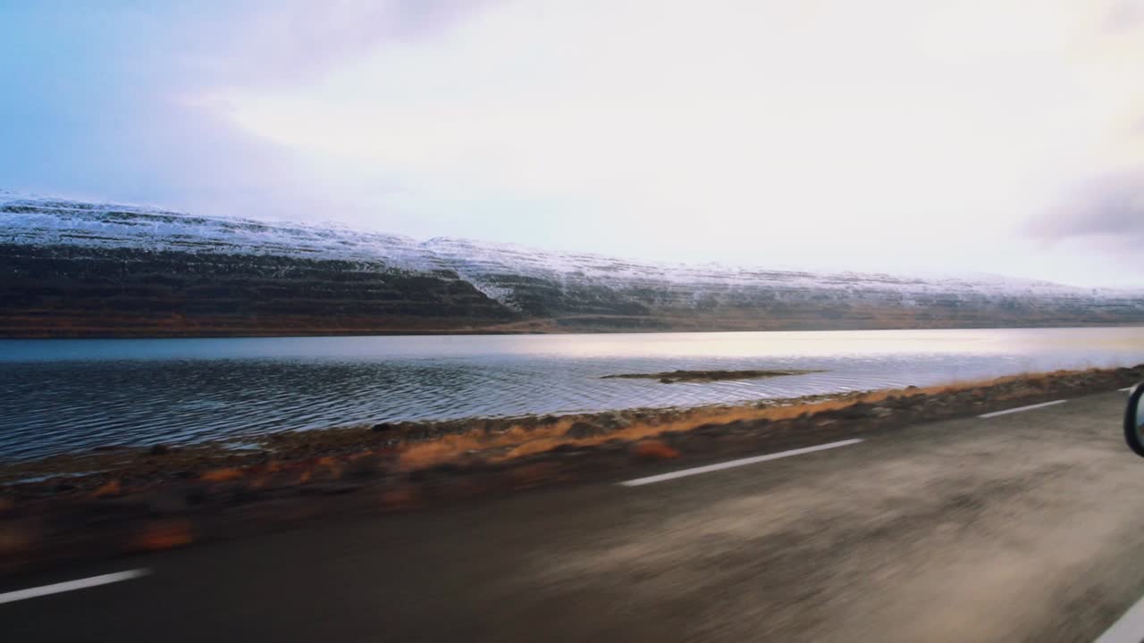 Udsigt over en stor flod og sneklædte bjerge på Island under kørsel.