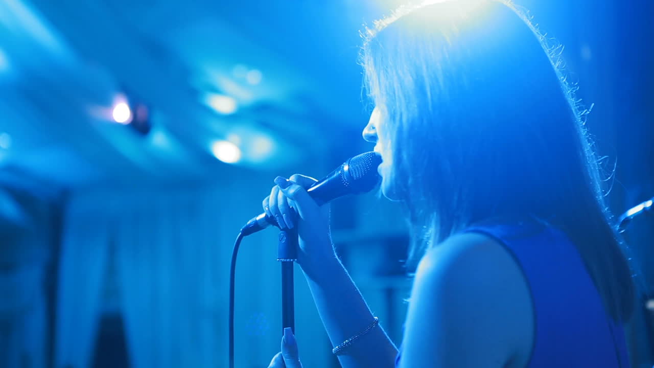 Beautiful girl with microphone singing on a concert with disco spotlights on the background