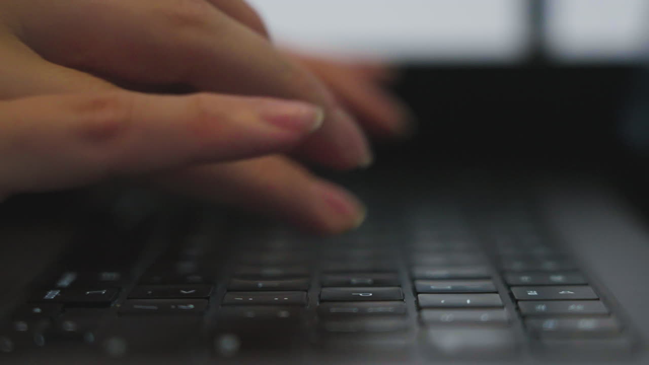 Slow motion side on shot of a woman's hands wearing rings typing on a keyboard