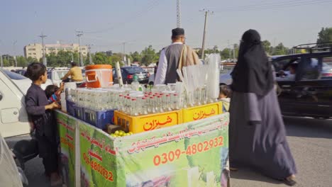 a child street vendor is selling fresh lemon soda on a cart in a busy public marketplace, and people are walking in the background.