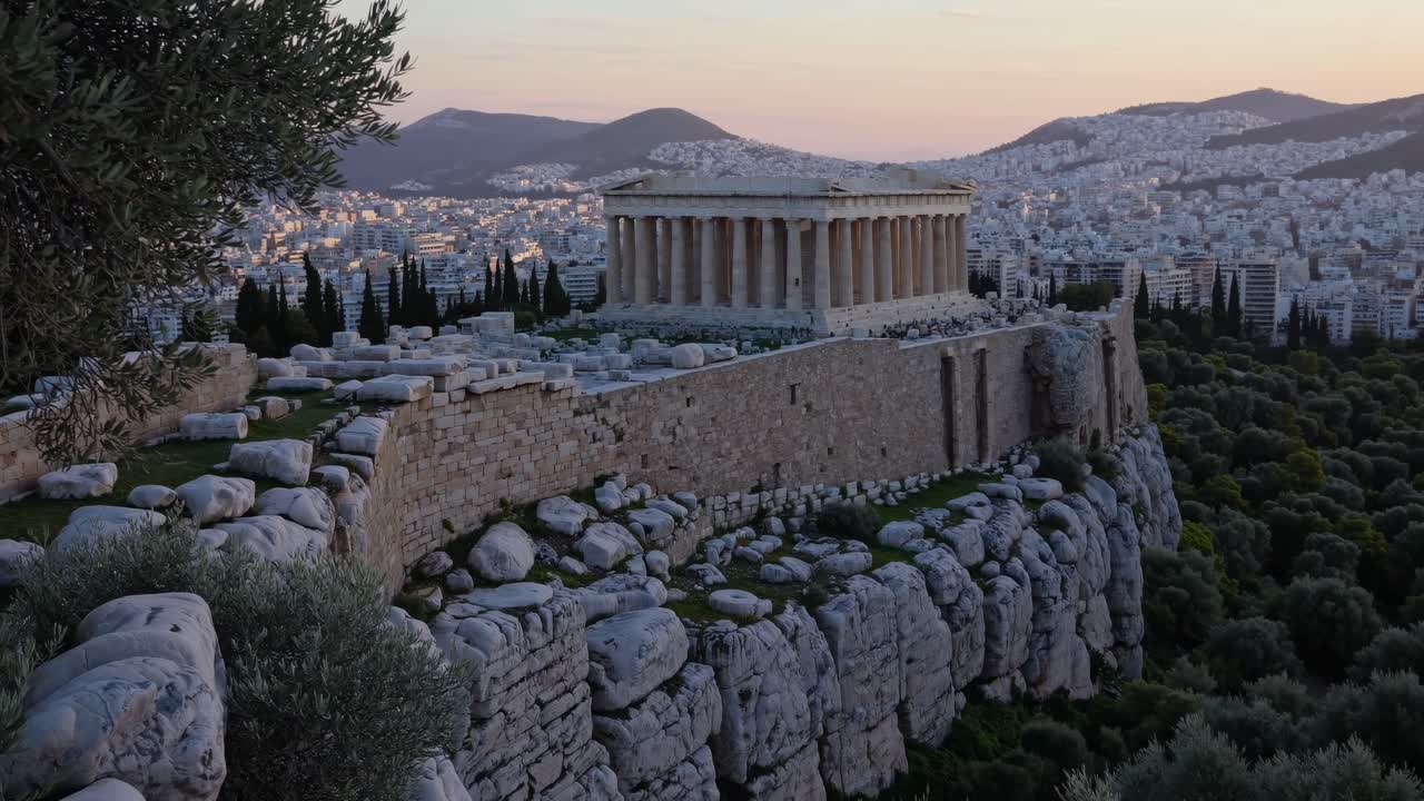 Vista aerea di antiche rovine in cima a una collina rocciosa al tramonto, con vista su un vasto paesaggio urbano
