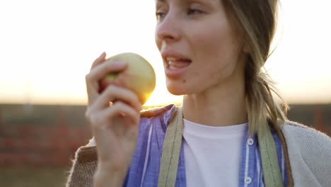 young woman cleans and biting a ripe red apple. organic food and gardening concept