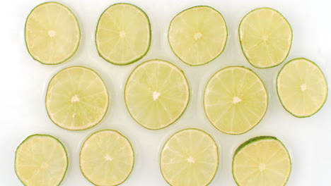 Splashes-of-water-fall-on-sliced-lime-green-rings-on-a-white-background.-Super-slow-motion.