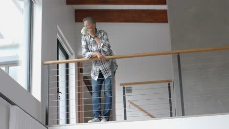 senior biracial man looking out of window, drinking coffee on staircase, copy space, slow motion