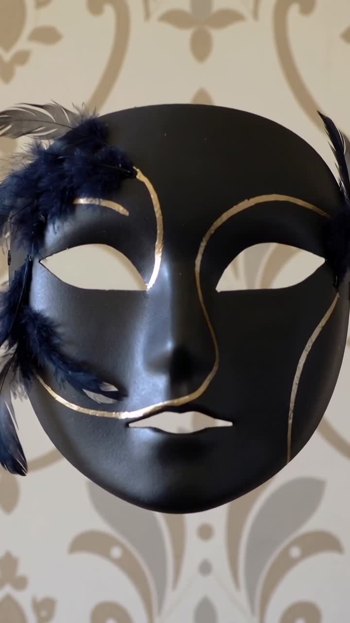Video verticale: La telecamera ingrandisce una maschera nera che rivela dettagli dorati e piume su una parete damascata.